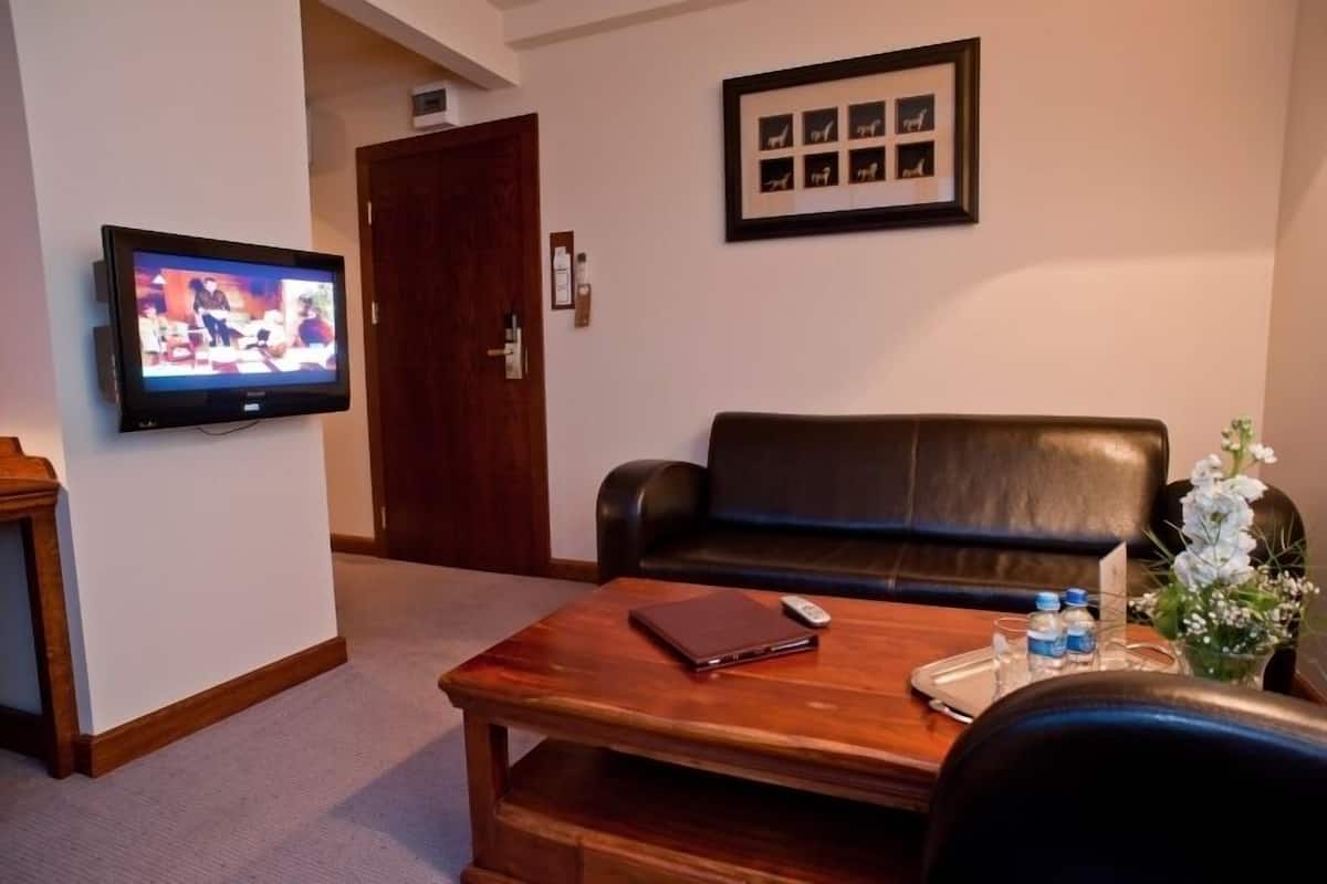 A room with a leather sofa, a wooden coffee table with a remote control and a notebook, a TV on the wall, and a framed photo collage.
