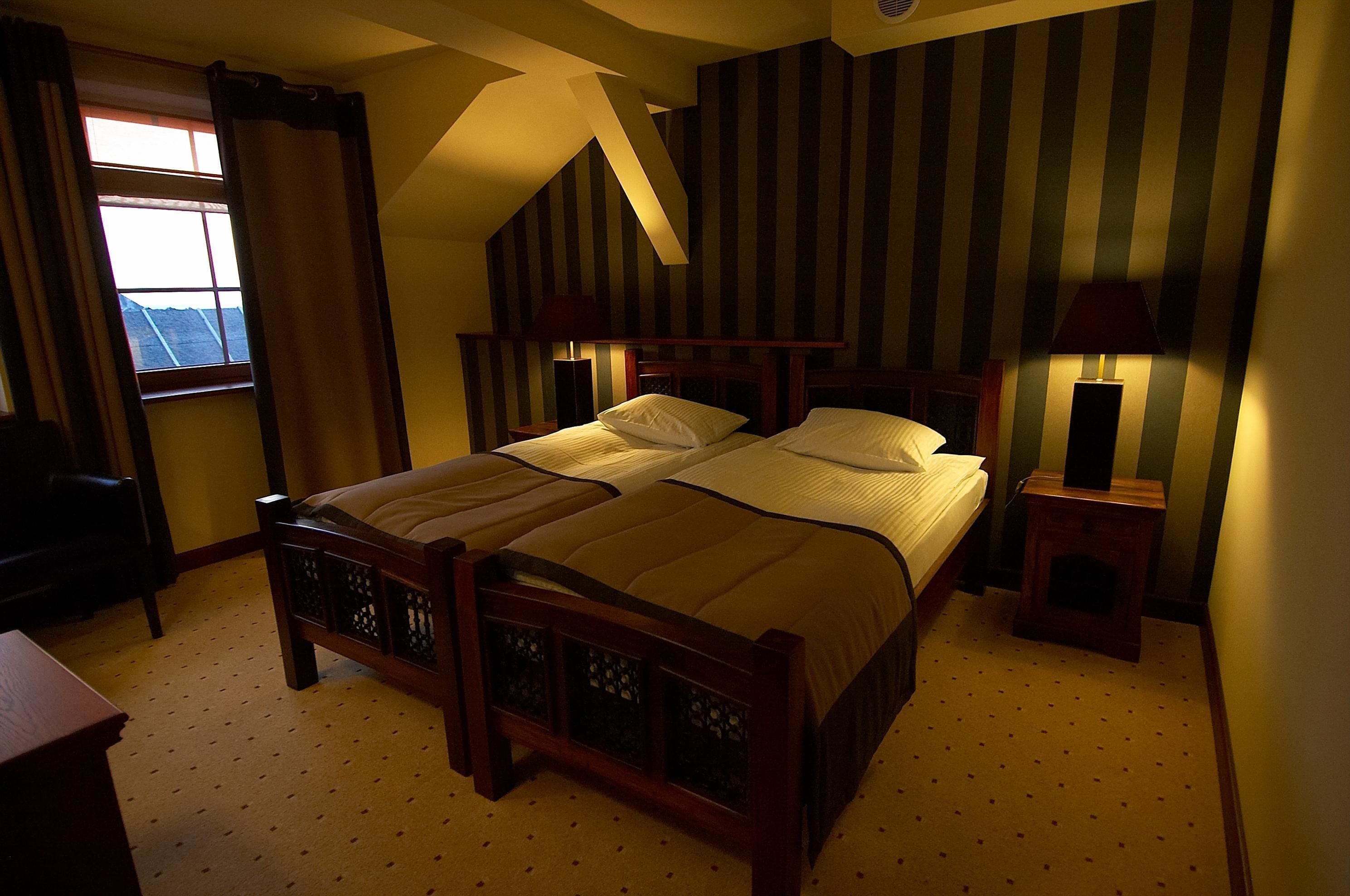 Een slaapkamer met een tweepersoonsbed, twee nachtkastjes met lampen, een raam met gordijnen en een schuin plafond.