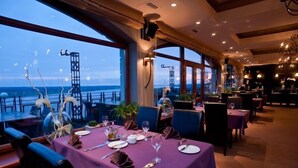 A restaurant with tables set for dining, large windows offering a view of the sea, and a modern interior design.