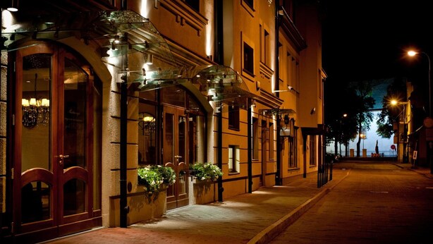 A nighttime street view of a row of buildings with a glass-fronted entrance and a wooden door.