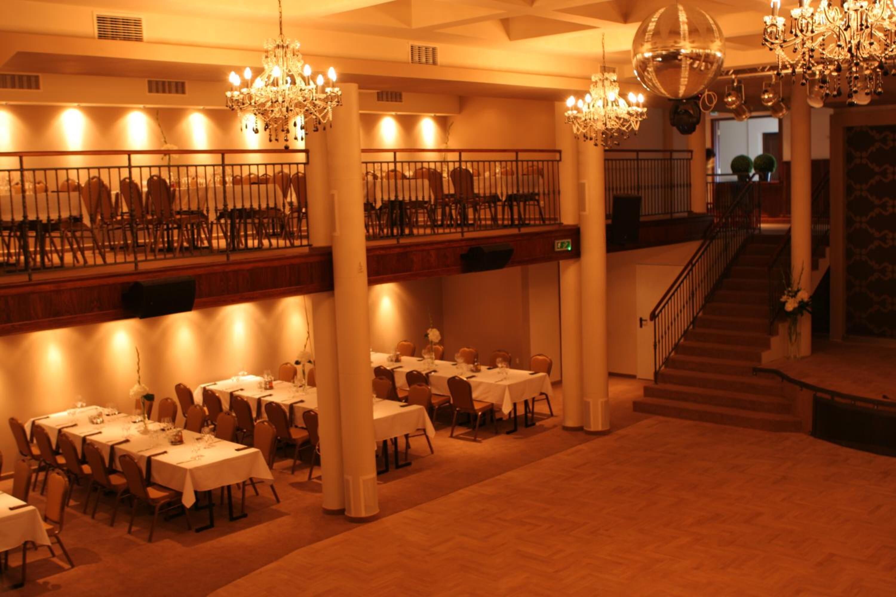A spacious dining area with multiple tables and chairs, a staircase, and a chandelier.
