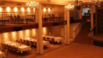 A spacious dining area with multiple tables and chairs, a staircase, and a chandelier.