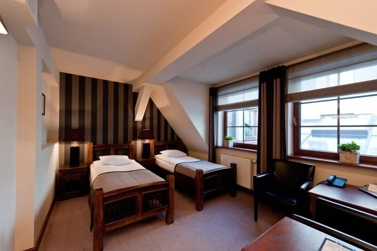 A hotel room with two beds, a desk, a chair, a window with a view, and a radiator.