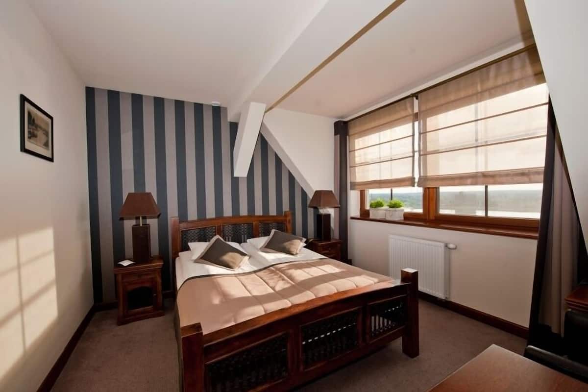 A bedroom with a wooden bed, striped wallpaper, a window with a view, and a radiator.