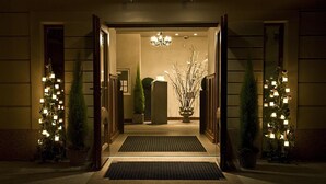 A hotel entrance with a chandelier, potted plants, and a welcoming mat.