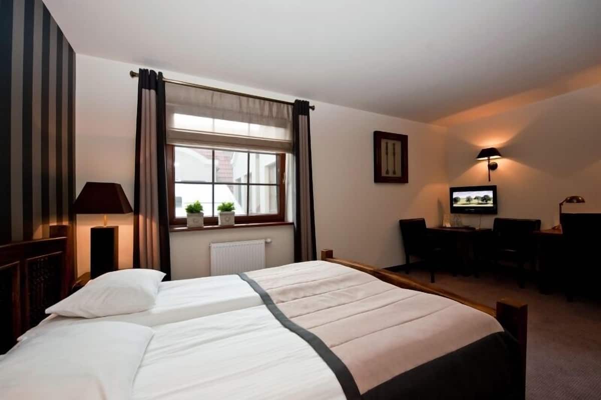 A hotel room with two beds, a desk, a chair, a television, and a window with curtains.