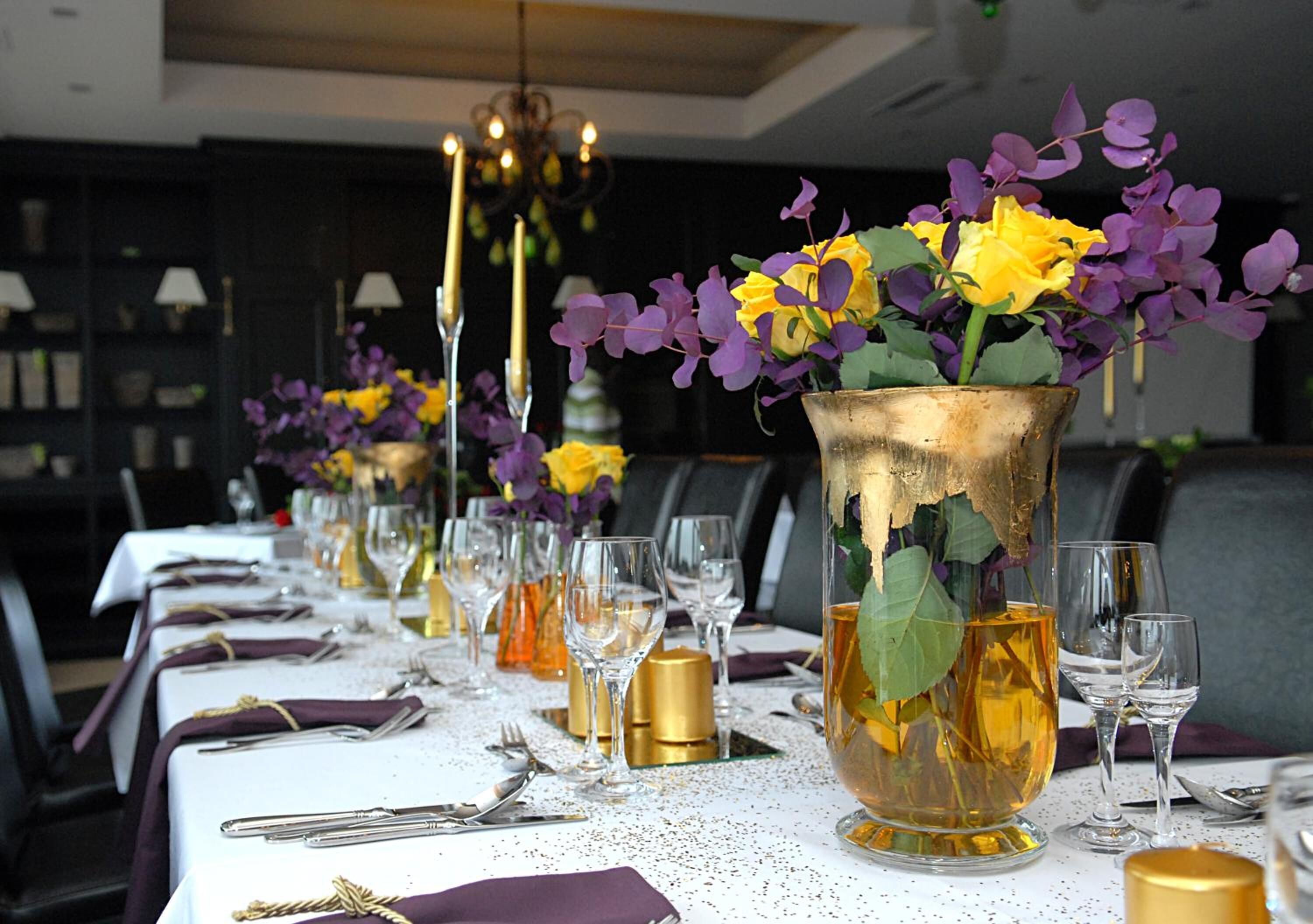 A long dining table set with multiple vases of flowers, wine glasses, and cutlery.