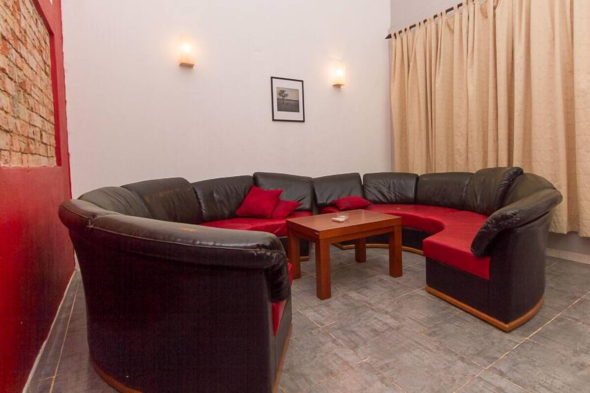 A corner living room with a black leather sofa, a wooden coffee table, and a red cushion. There are two wall-mounted lights and a framed picture on the wall.