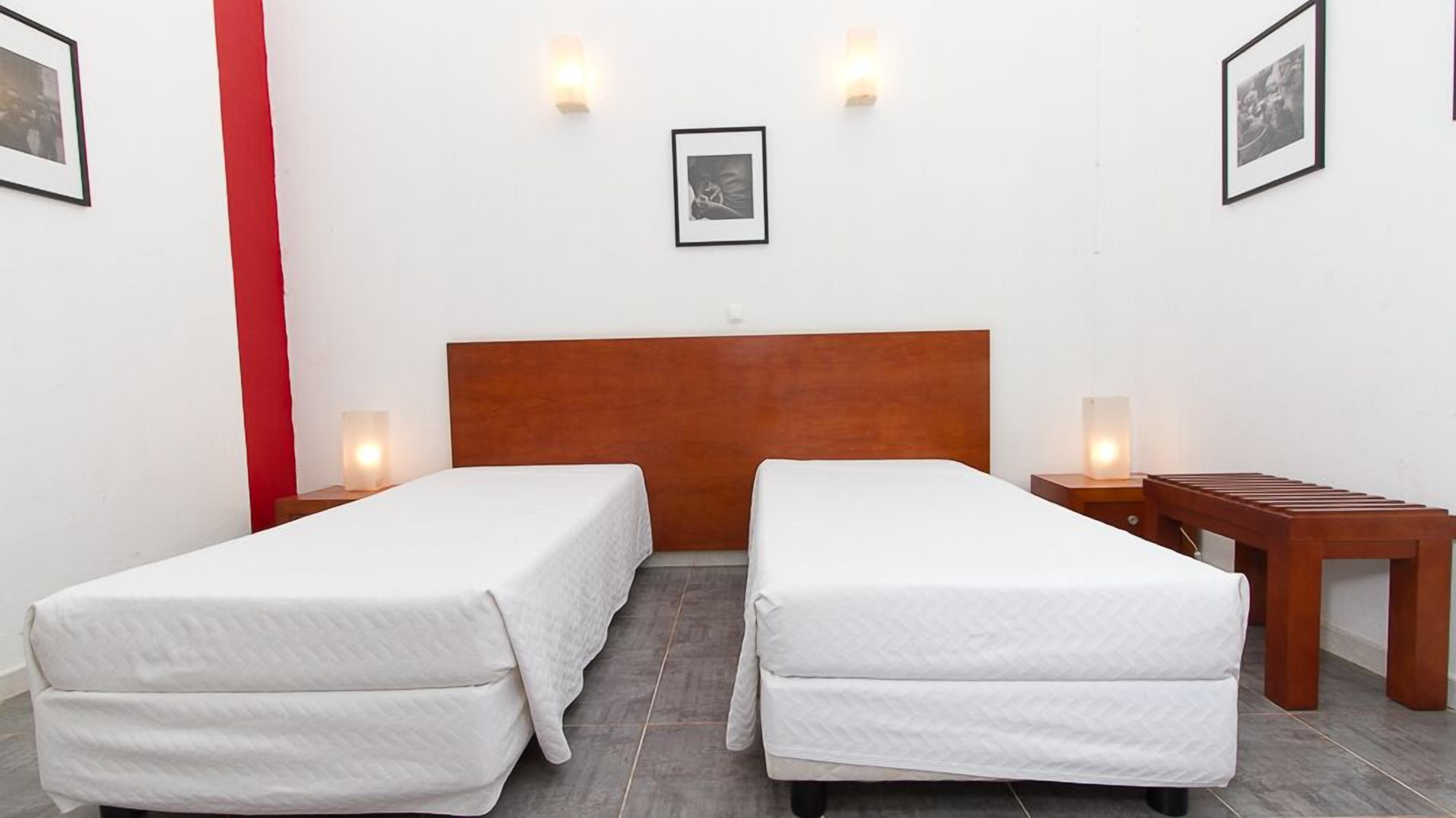 Een hotelkamer met twee eenpersoonsbedden, een houten hoofdbord, nachtkastjes met lampen en ingelijste foto's aan de muur.