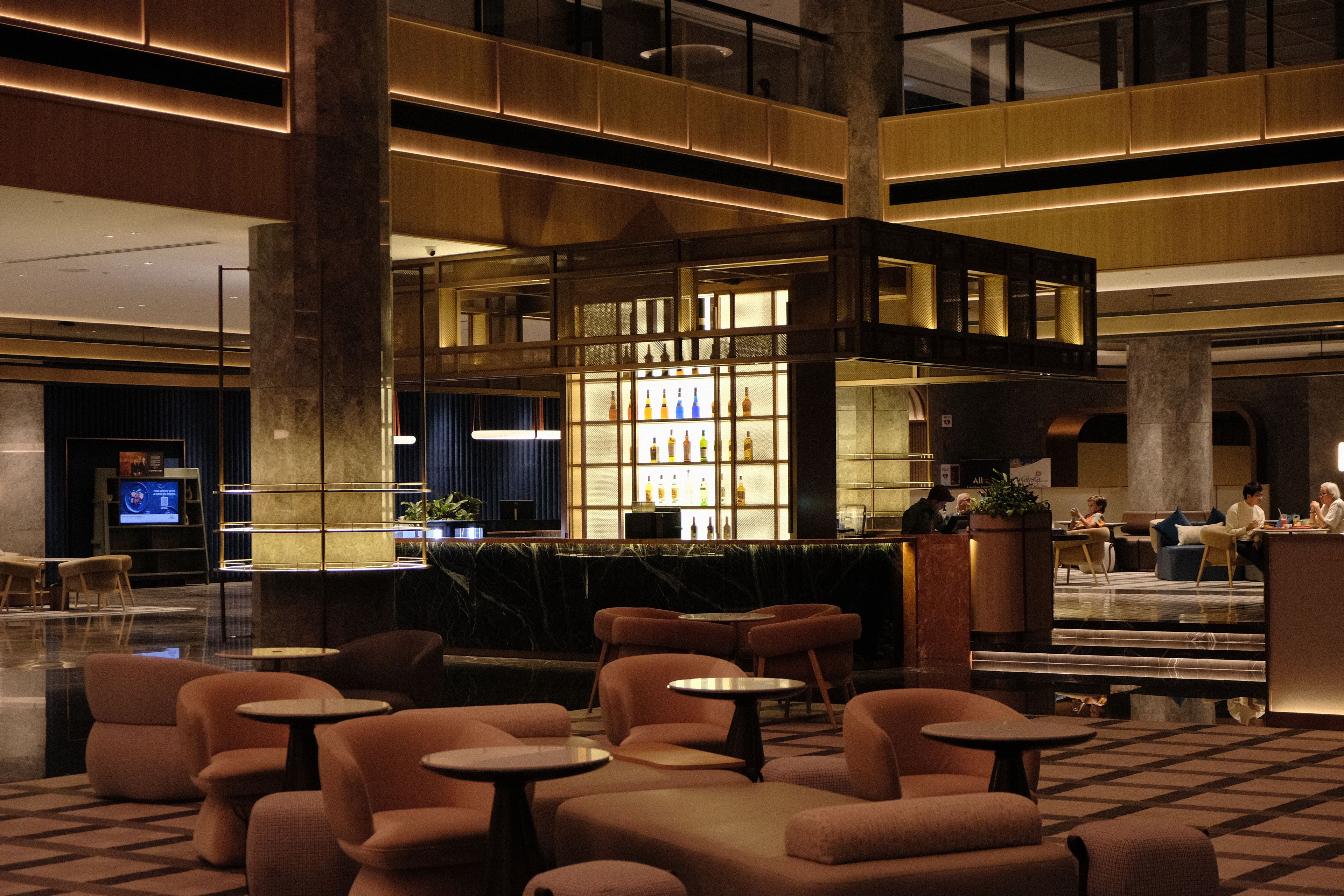 A spacious lobby with a bar area, seating arrangements, and a large digital screen.