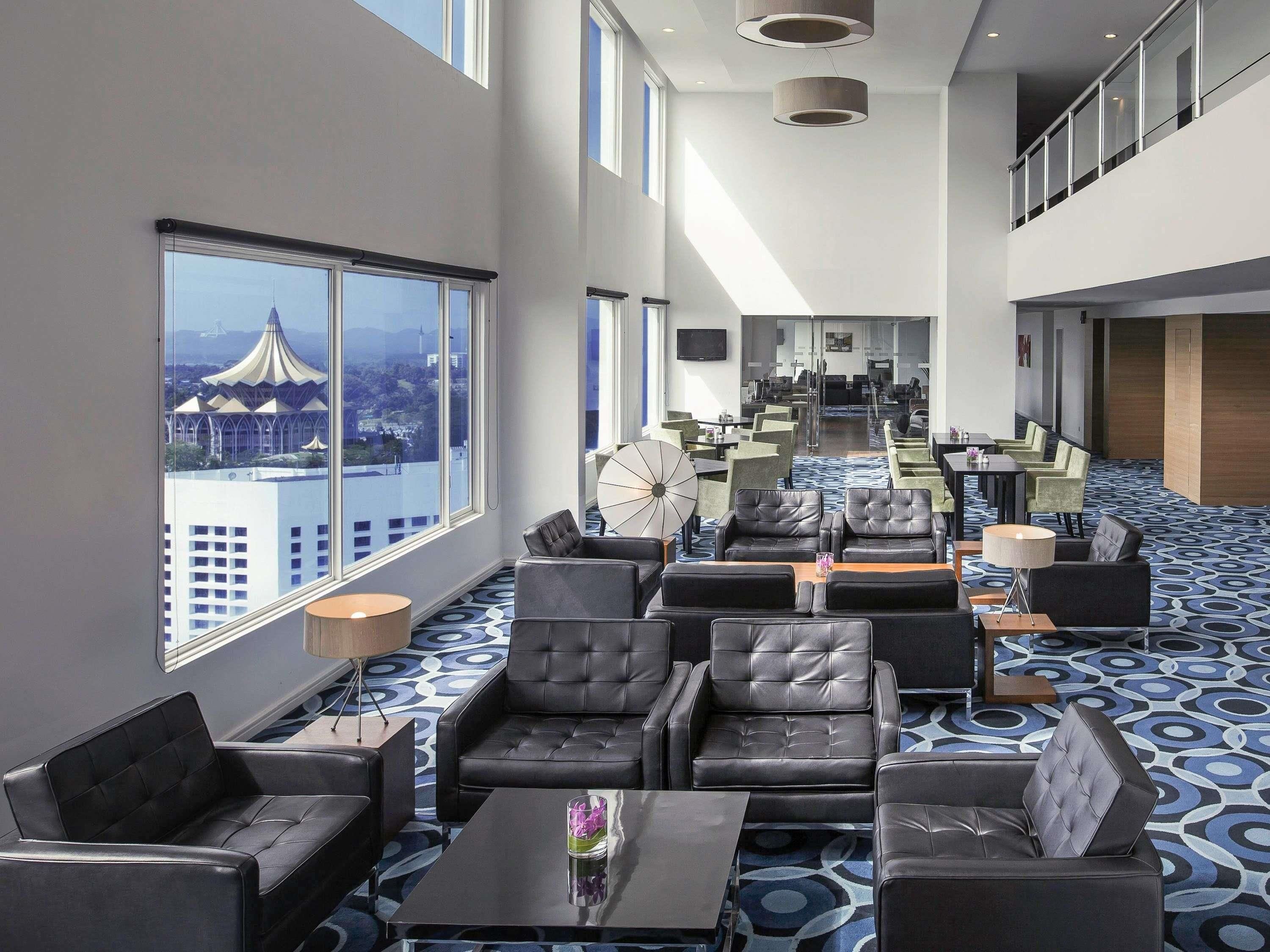 A hotel lobby with a high ceiling, large windows, and a view of a cityscape.