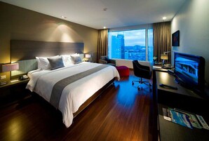Una habitación de hotel moderna con una cama grande, un escritorio con computadora, un televisor y vistas a la ciudad.