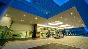 A modern hotel entrance with a glass facade, a car parked outside, and a tall building in the background. - Pullman Kuching (Kuching)