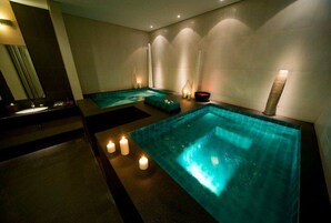Un área de spa con un amplio jacuzzi rectangular, velas y una pequeña zona de estar.
