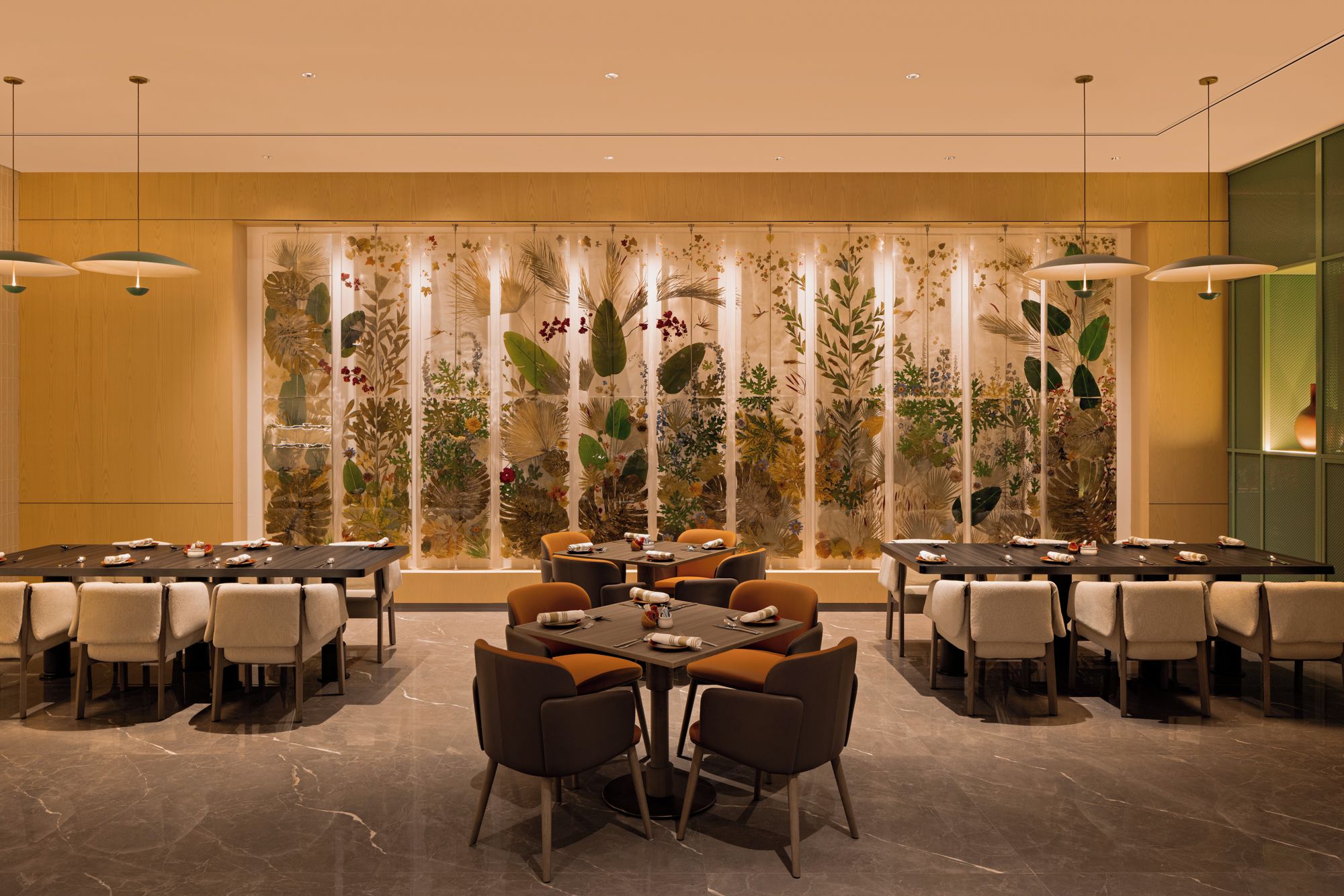 A modern dining area with multiple tables and chairs, a decorative plant wall, and pendant lighting.