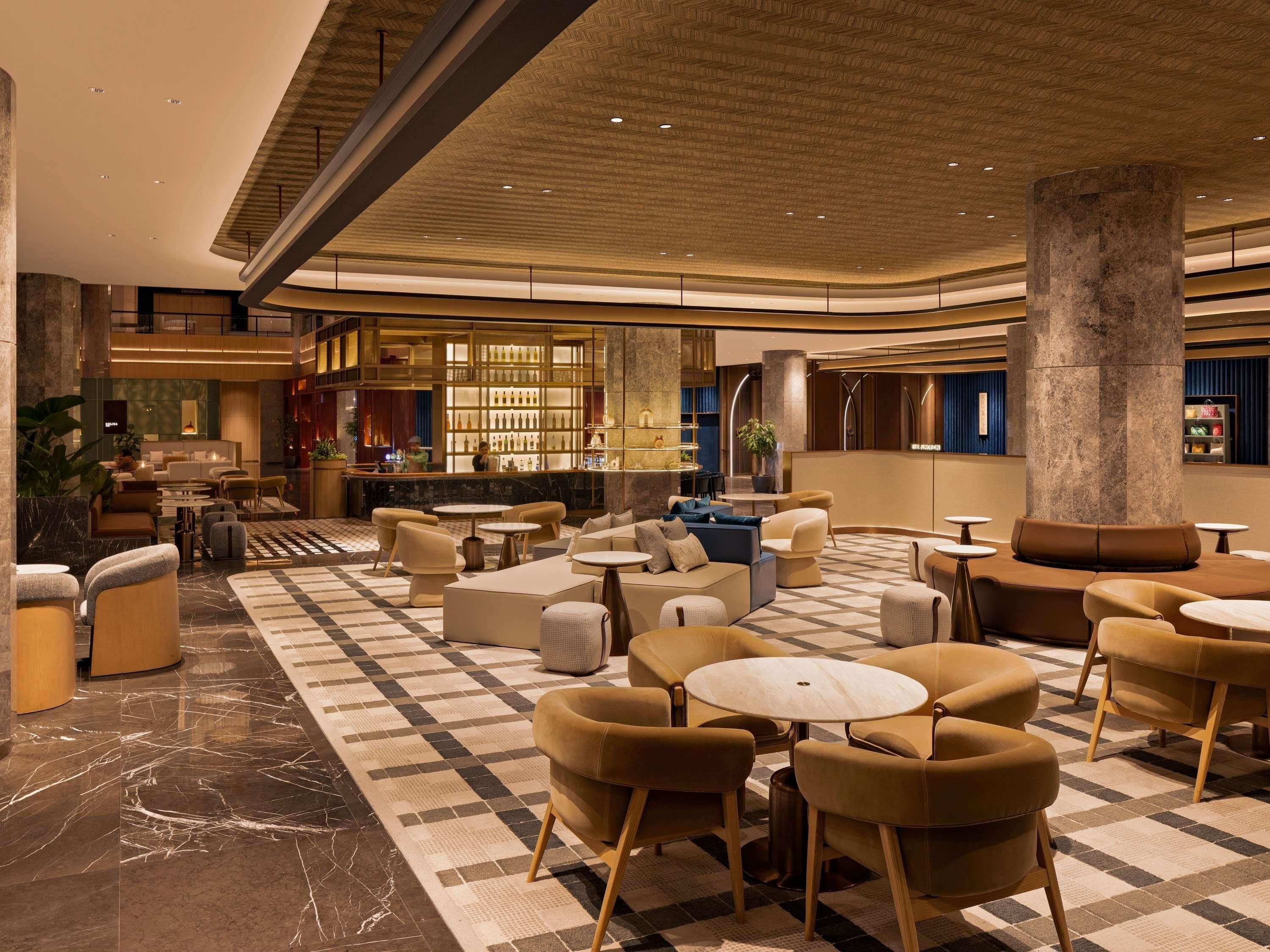 A spacious lobby with a checkered floor, seating areas, a bar, and a large column.