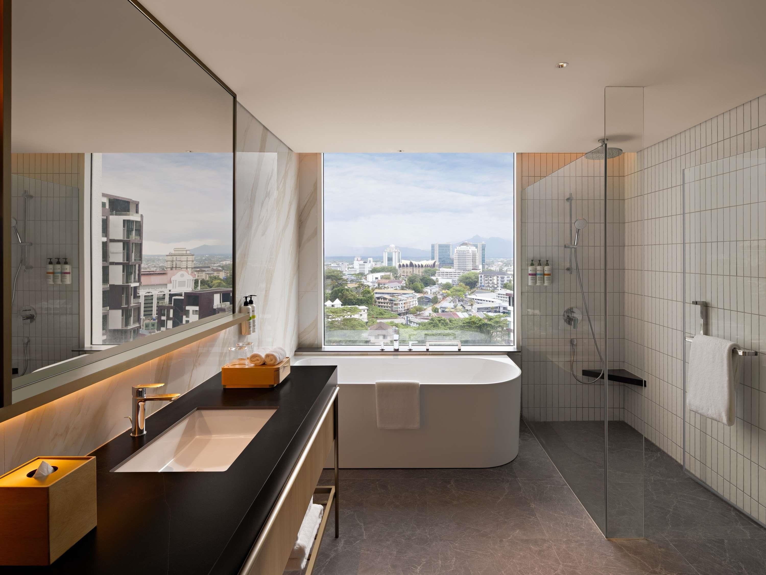 A modern bathroom with a large bathtub, a glass-enclosed shower, and a city view.