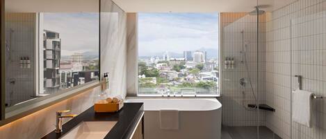 A modern bathroom with a large bathtub, a glass-enclosed shower, and a city view.