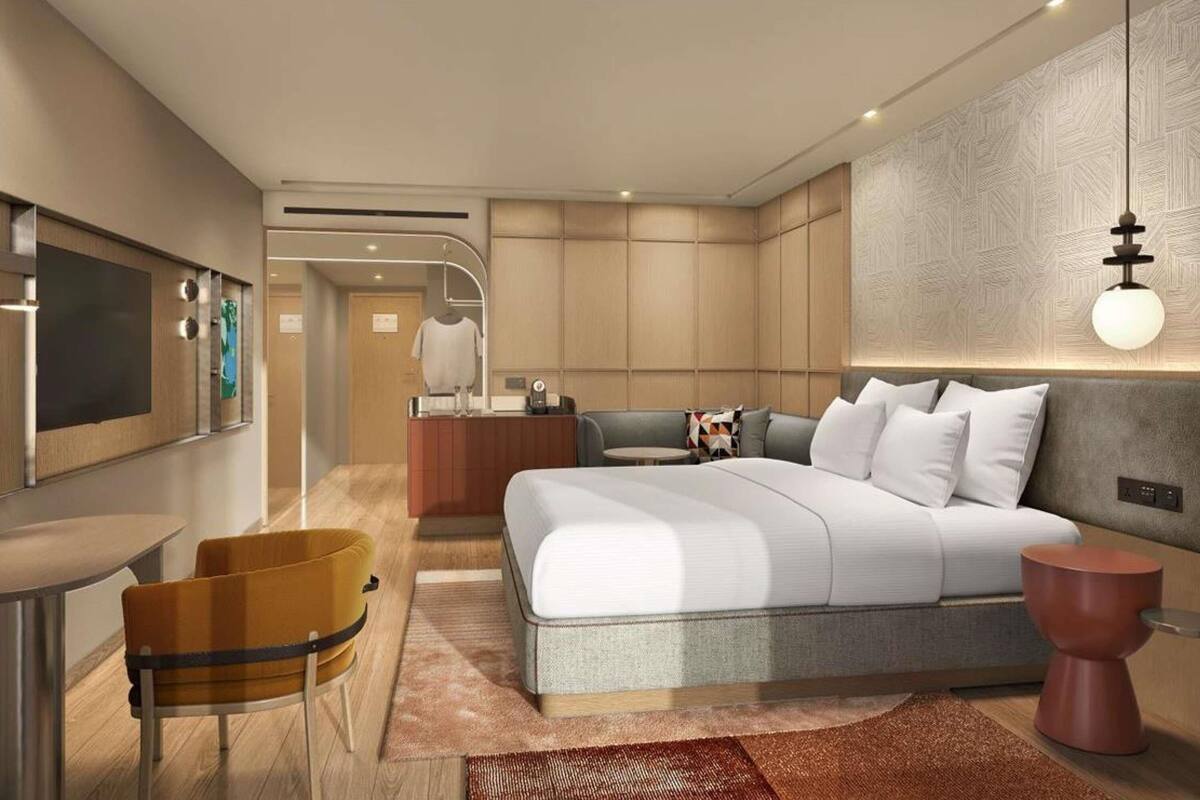 A modern hotel room with a bed, a small table, a chair, a mirror, and a hanging light fixture.