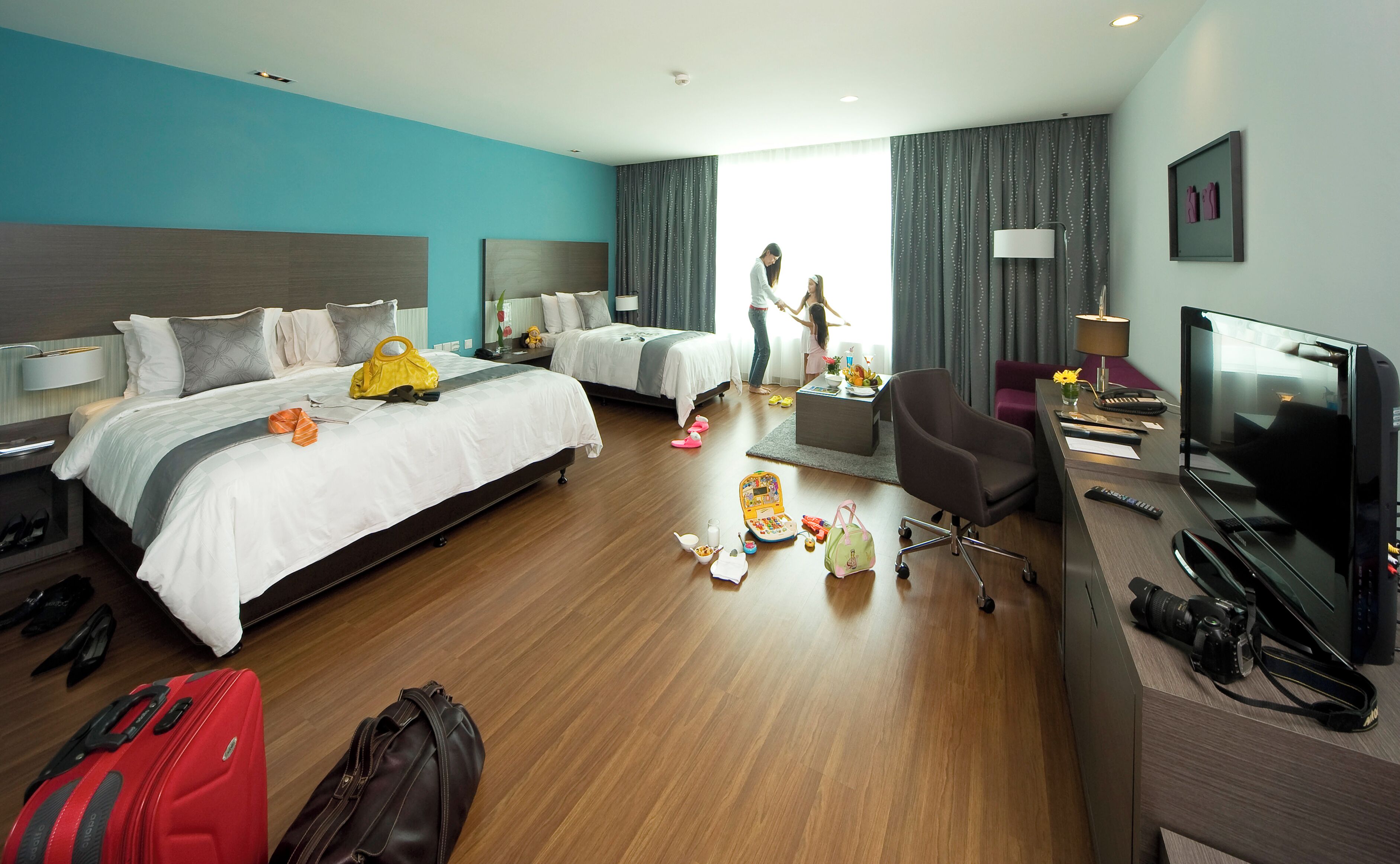 Habitación de hotel con dos camas, un escritorio con televisor, una silla y espacio para equipaje.