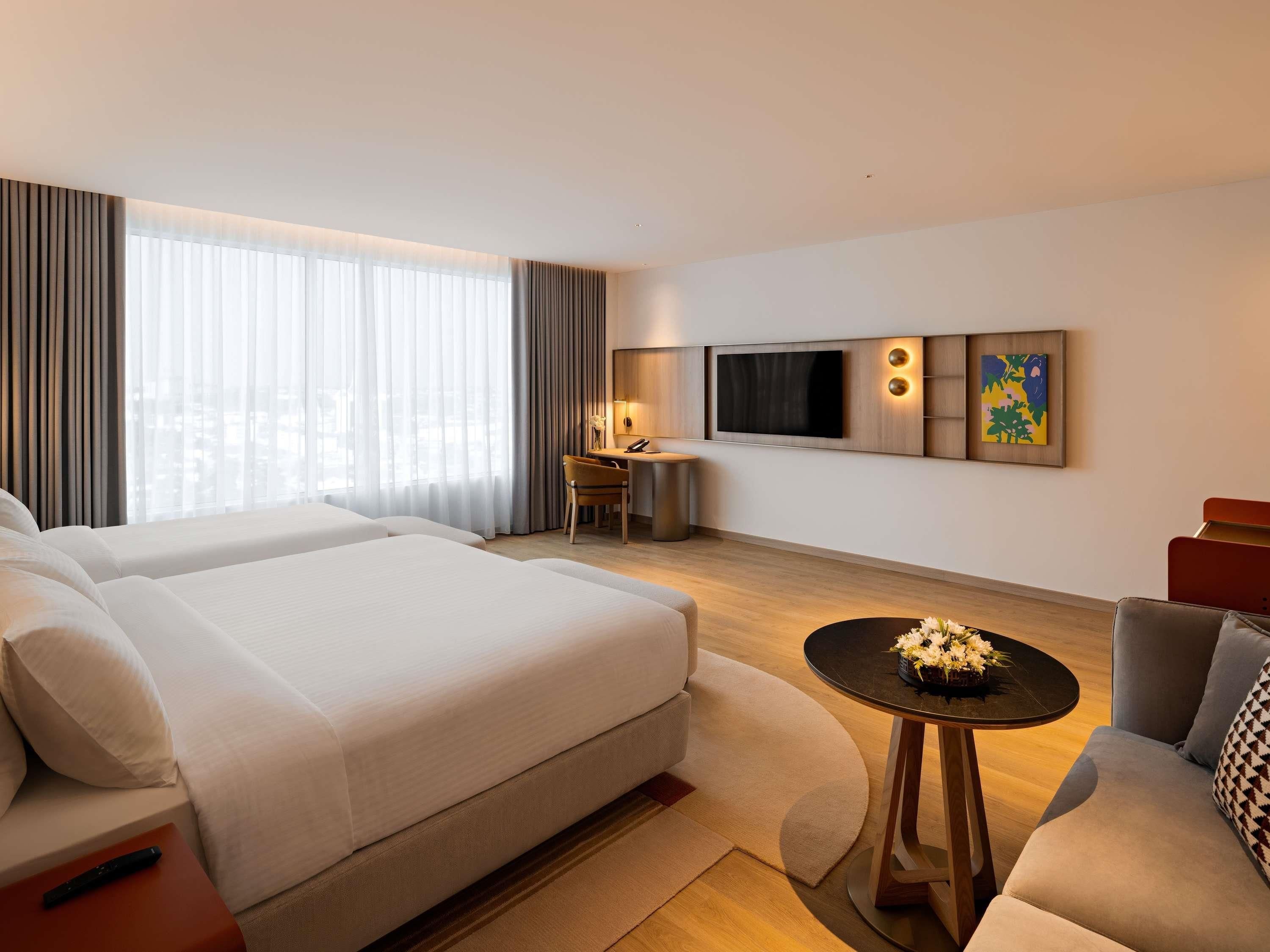A hotel room with two beds, a desk, a TV, and a sofa.
