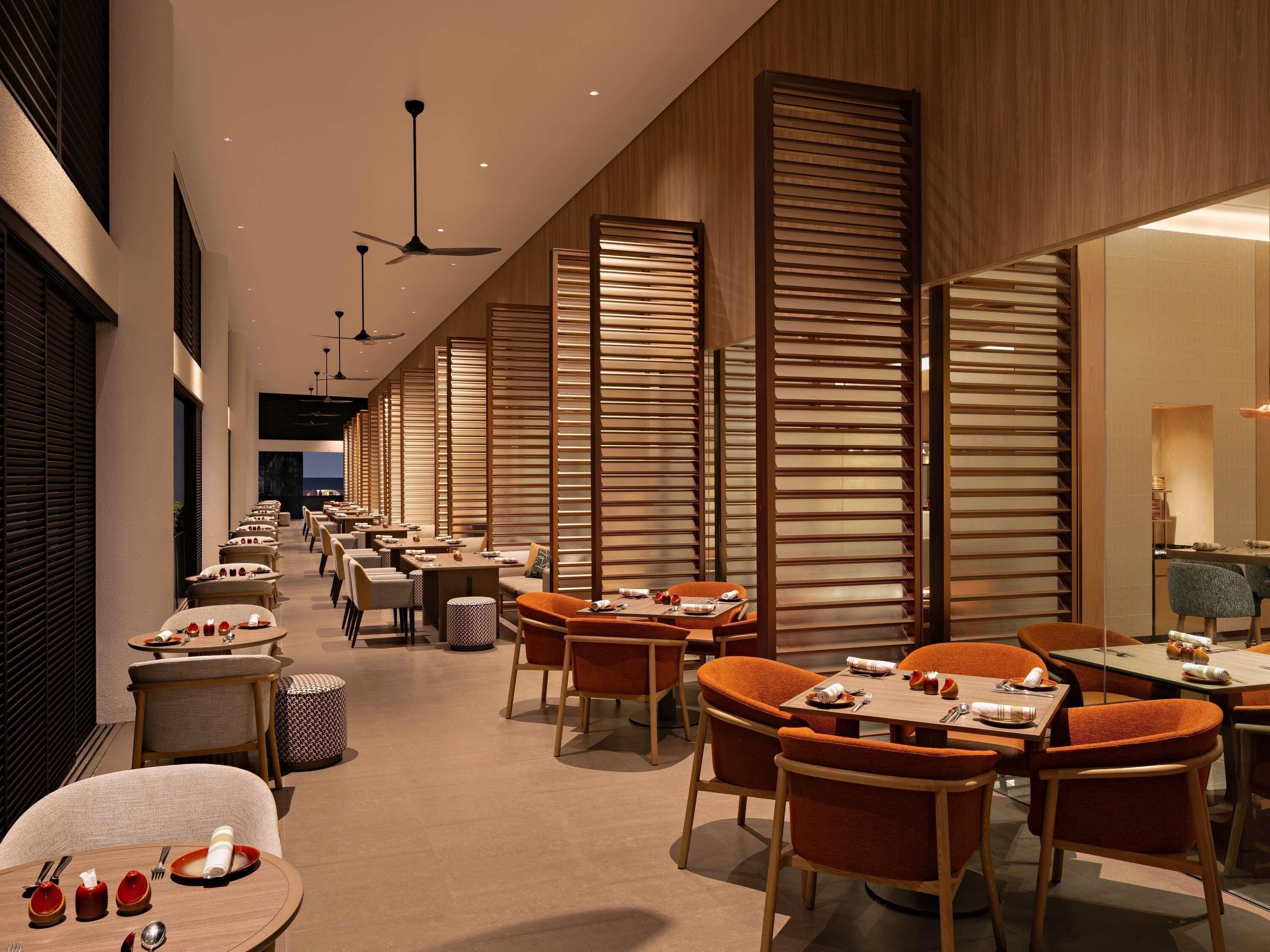 A modern restaurant with multiple tables and chairs, ceiling fans, and wooden partitions.