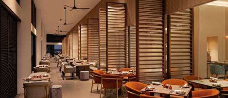 A modern restaurant with multiple tables and chairs, ceiling fans, and wooden partitions.