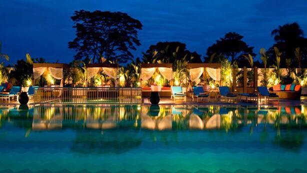 A nighttime pool area with lounge chairs and umbrellas, surrounded by palm trees and a gazebo. - Pullman Kuching (Kuching)