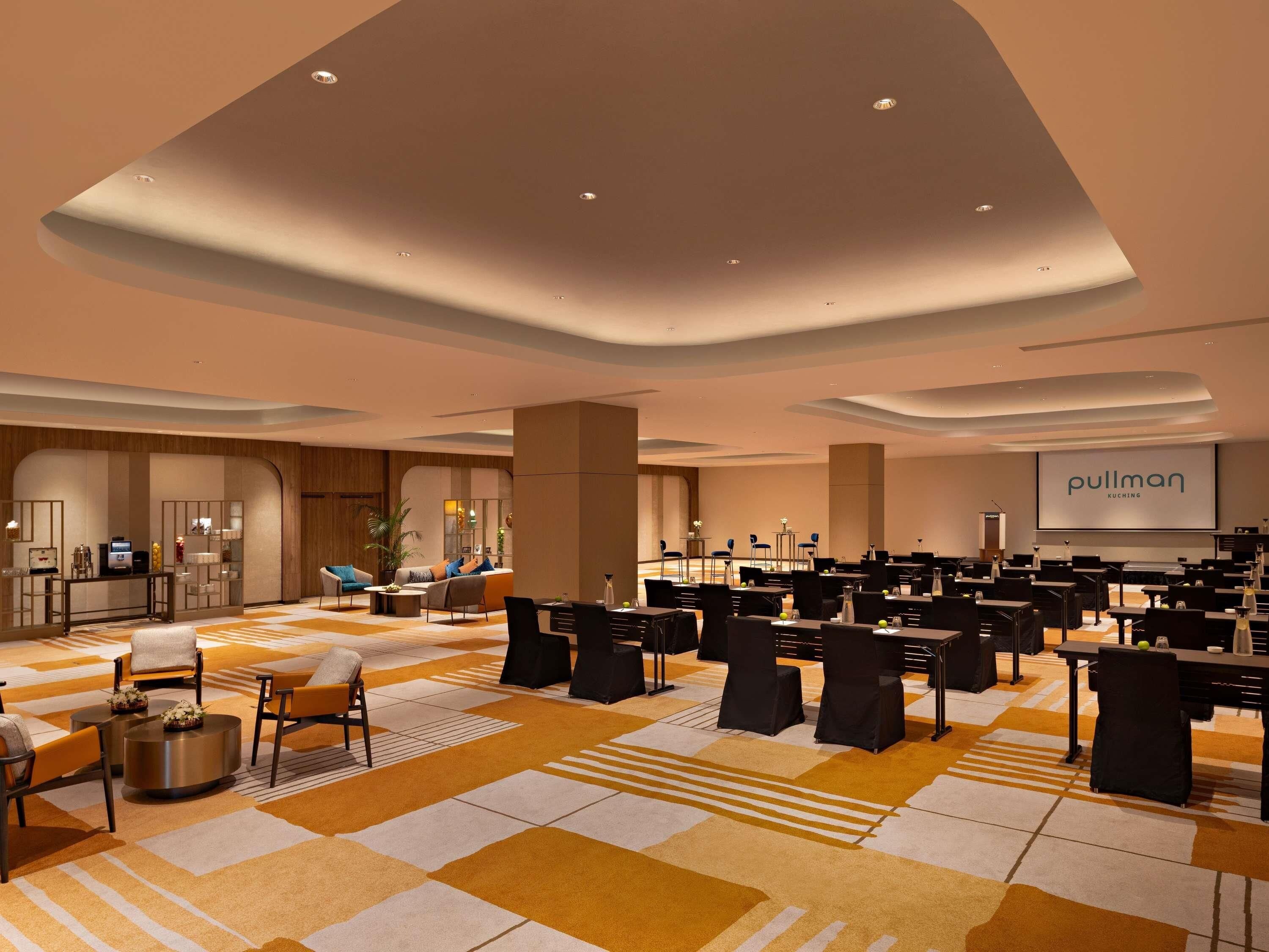 A hotel conference room with a stage, seating, and a large screen displaying 'pullman'.