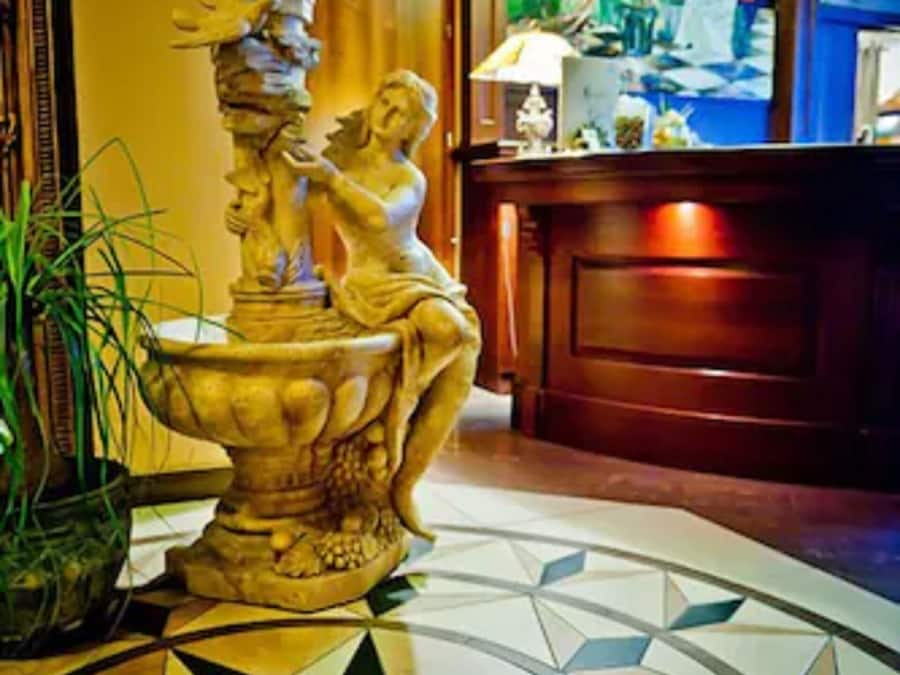 Un vestíbulo con una fuente decorativa, piso estampado y una recepción con lámpara.