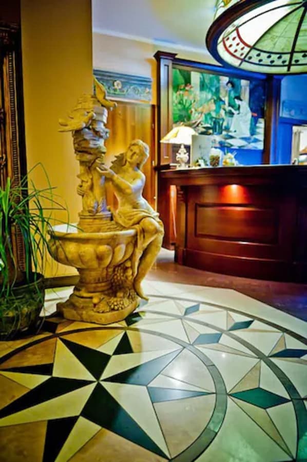 A lobby with a decorative fountain, a patterned floor, and a reception desk with a lamp.