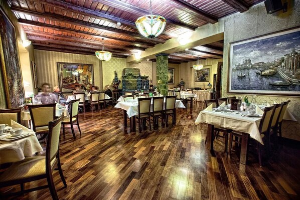 A restaurant with wooden flooring, tables set with white tablecloths, and hanging chandeliers. - Hotel Gaja (Poznan)