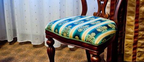 Una silla de madera con un cojín estampado en una habitación con alfombra estampada y una ventana con cortinas traslúcidas.