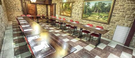 Une salle de conférence avec une longue table, des chaises rouges et des murs en pierre.
