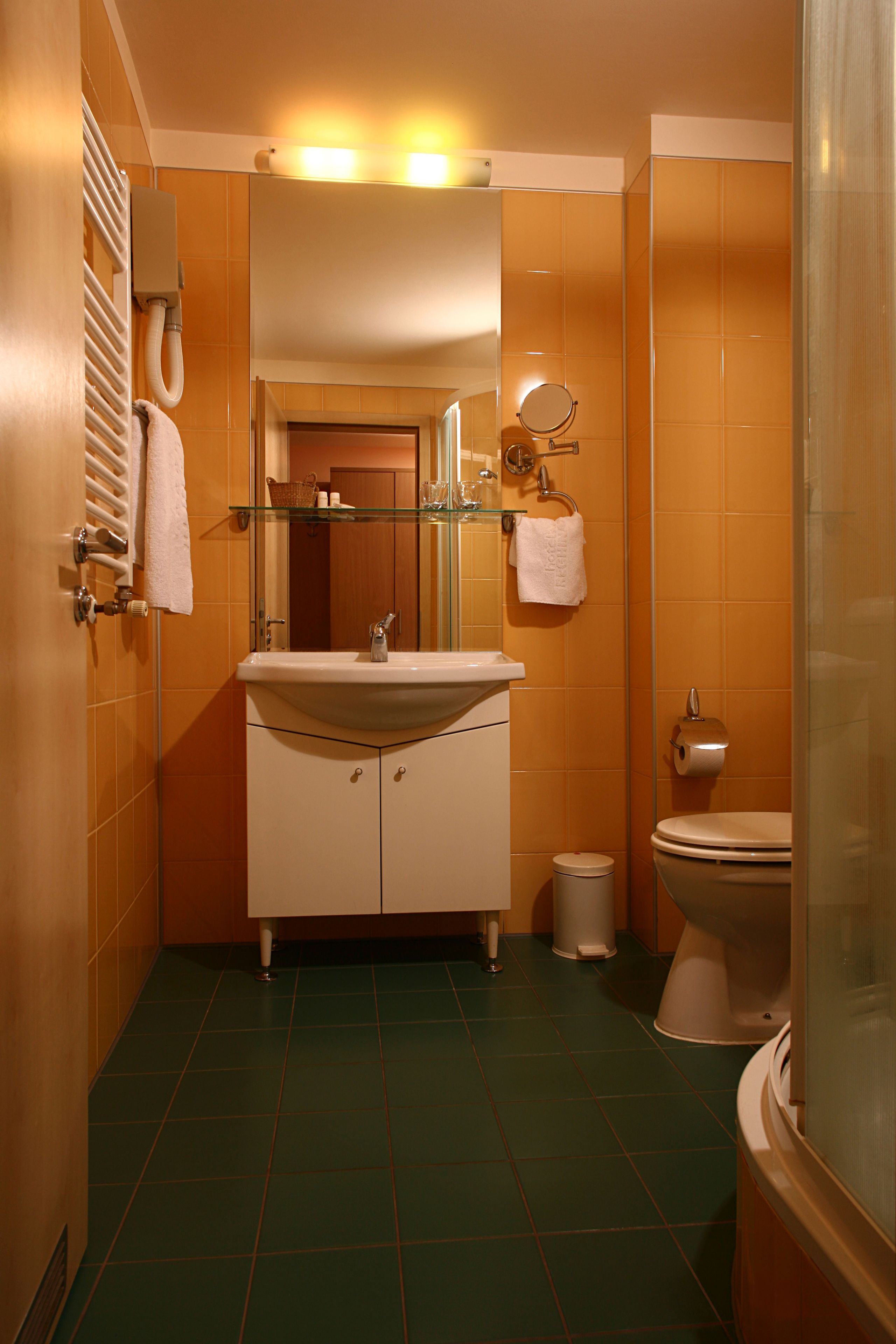 A bathroom with a sink, mirror, toilet, and a trash bin.