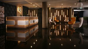 Un área de recepción moderna con un mostrador de madera, un logotipo y un espacio de espera con sillas blancas y anaranjadas.