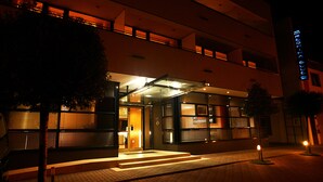 Entrada de hotel moderna con puerta de cristal, escalones que conducen a ella y fachada bien iluminada.