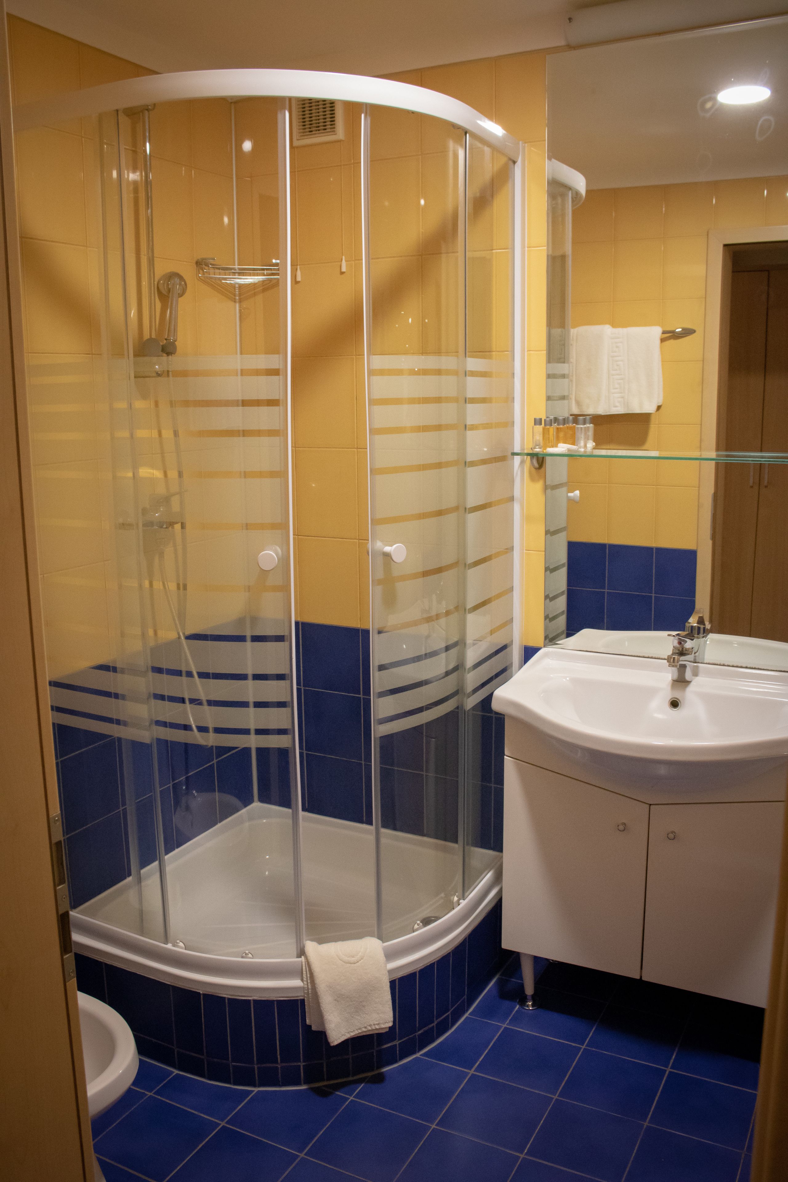 Un baño con cabina de ducha de vidrio, un lavamanos blanco y paredes con azulejos azules.