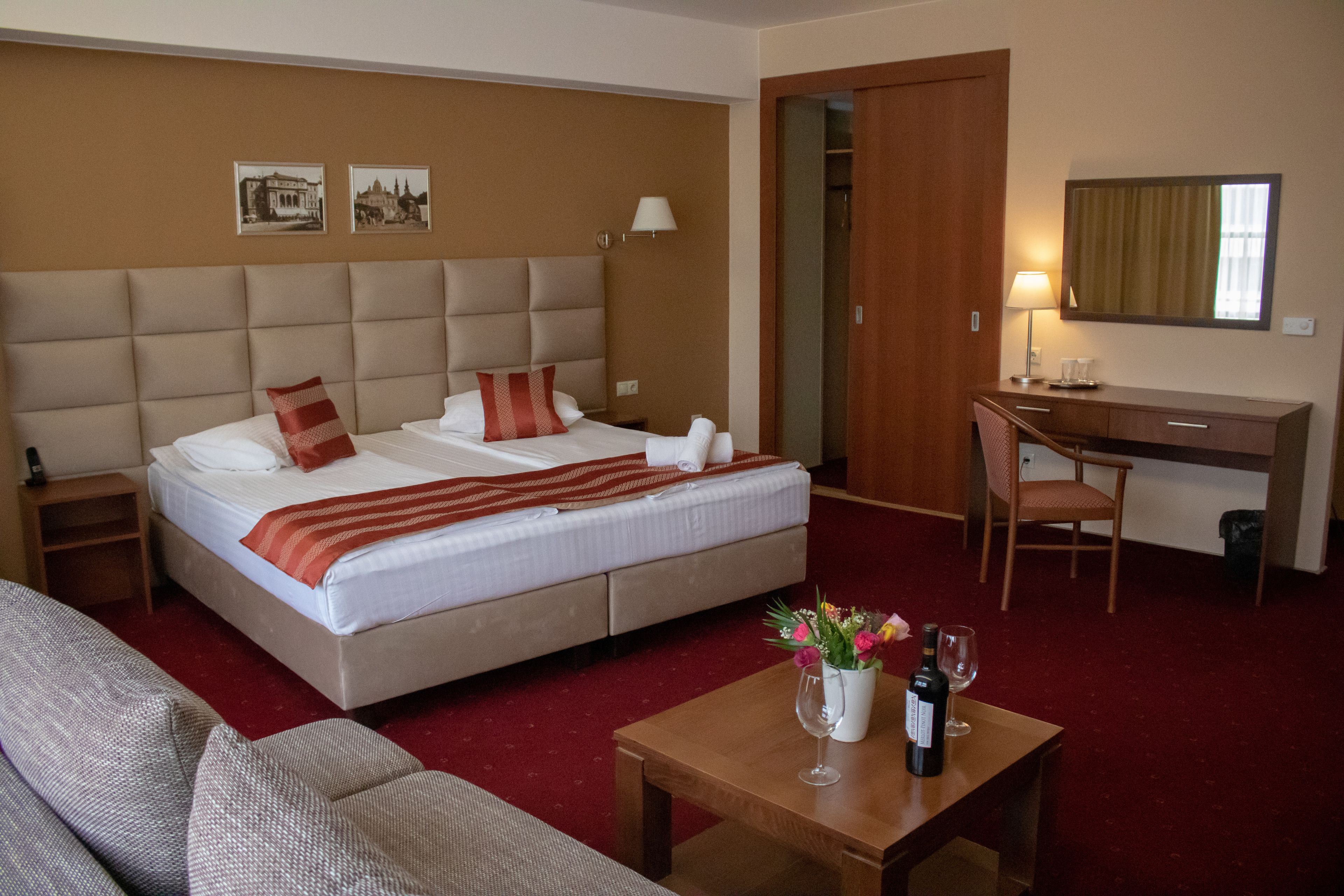 A hotel room with a large bed, a desk, a chair, a small table with a vase of flowers, and a mirror on the wall.