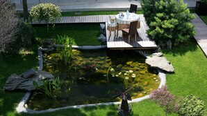 Un jardín con estanque, terraza de madera y zona de estar al aire libre.