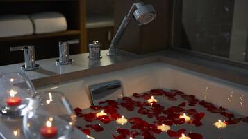 Un baño con una bañera llena de pétalos de rosa y velas, un cabezal de ducha y un perchero.