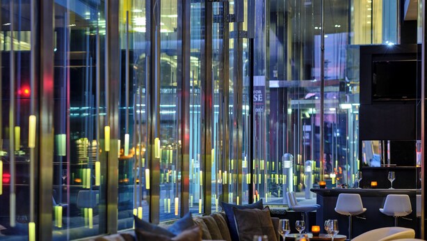 A modern interior with a seating area, tables, and a large window offering a city view. - Hotel Le Germain Calgary (Calgary)