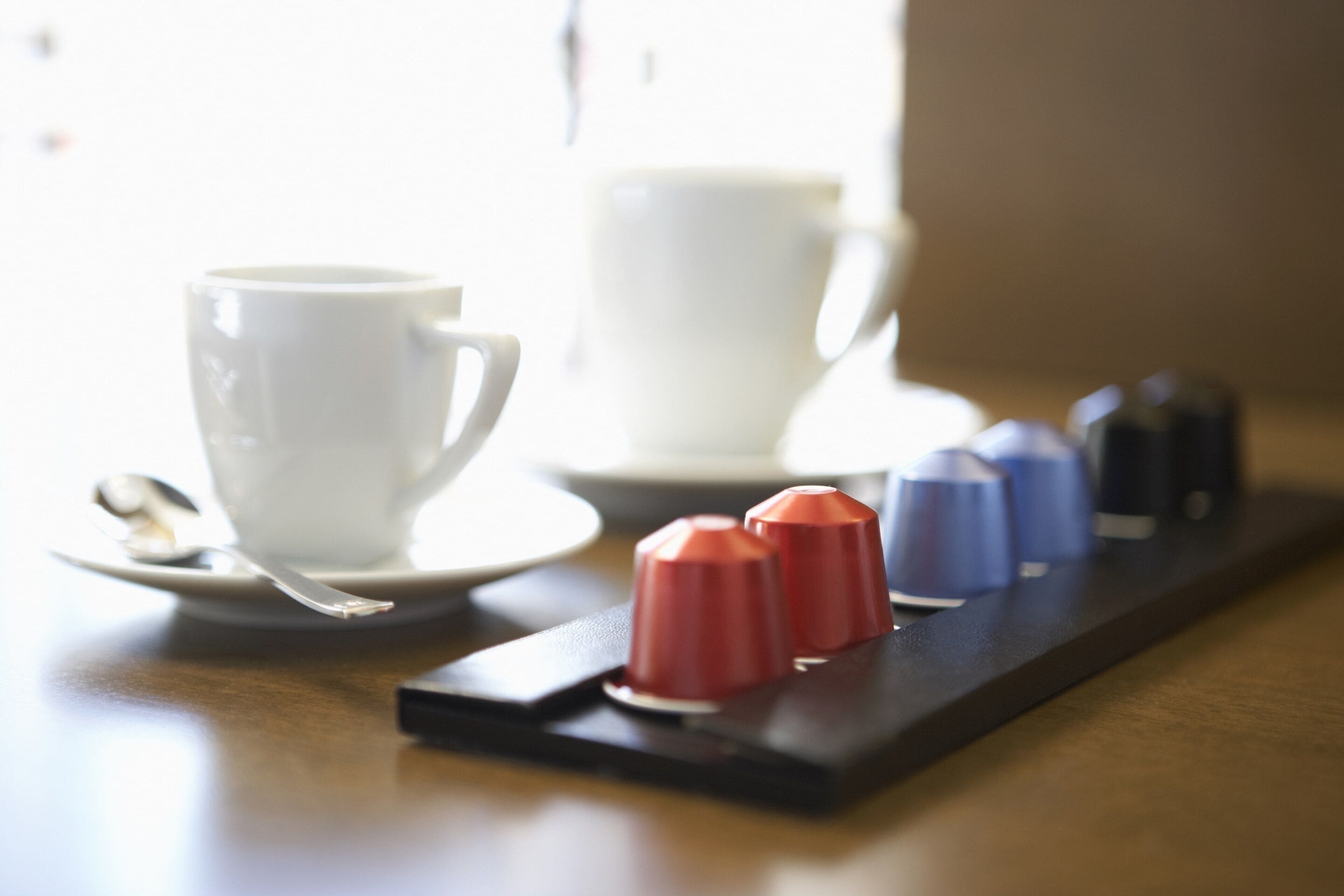 A tray with two red and two blue sugar cubes, a white cup, and a spoon on a table.