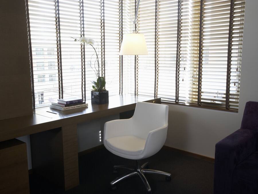 A modern office chair with a white seat and chrome legs, positioned in front of a desk with a lamp and a potted plant.