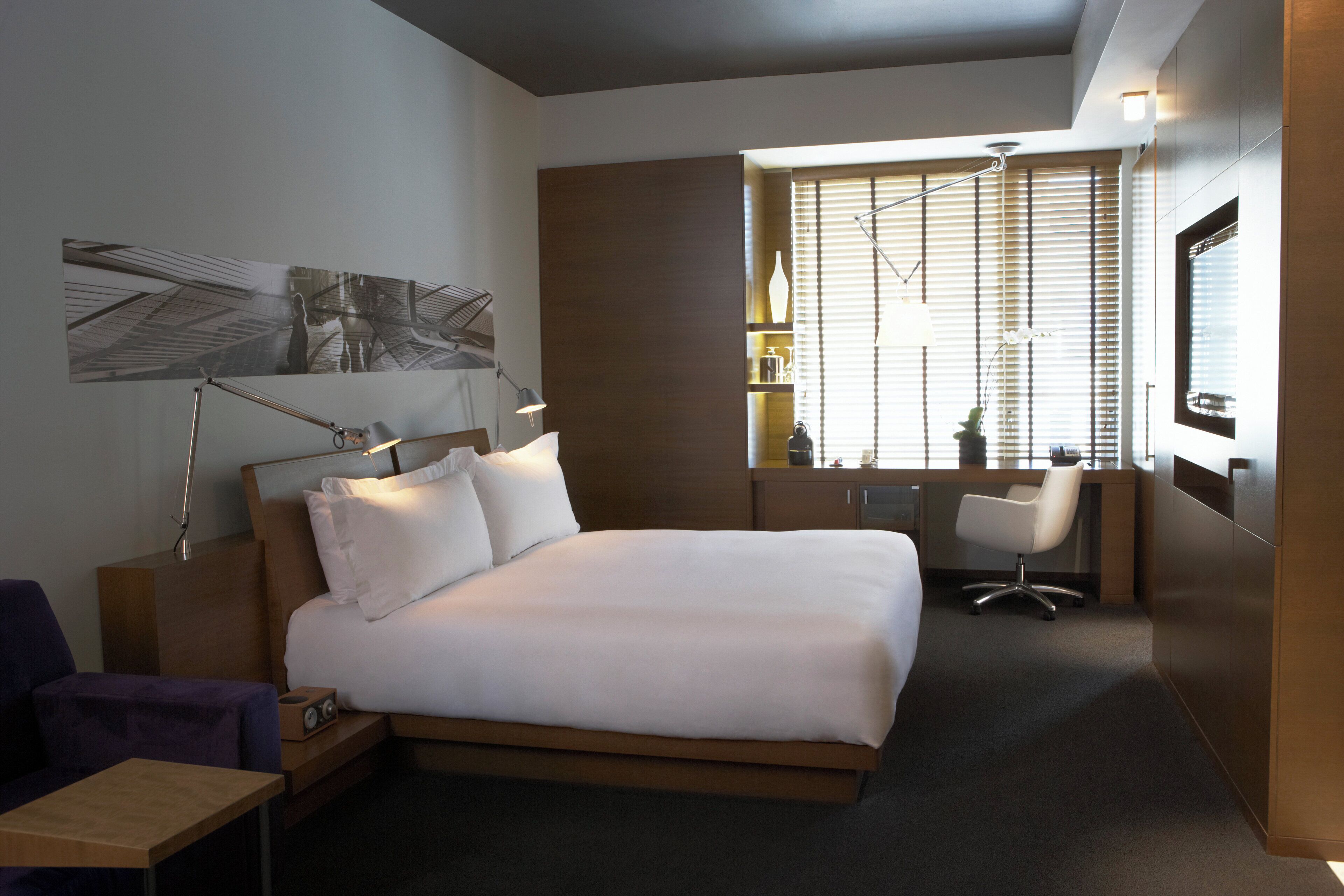 Una habitación de hotel moderna con una cama grande, mesita de noche, lámpara y escritorio con silla.