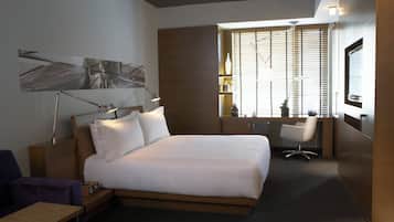 Una habitación de hotel moderna con una cama grande, mesita de noche, lámpara y escritorio con silla.