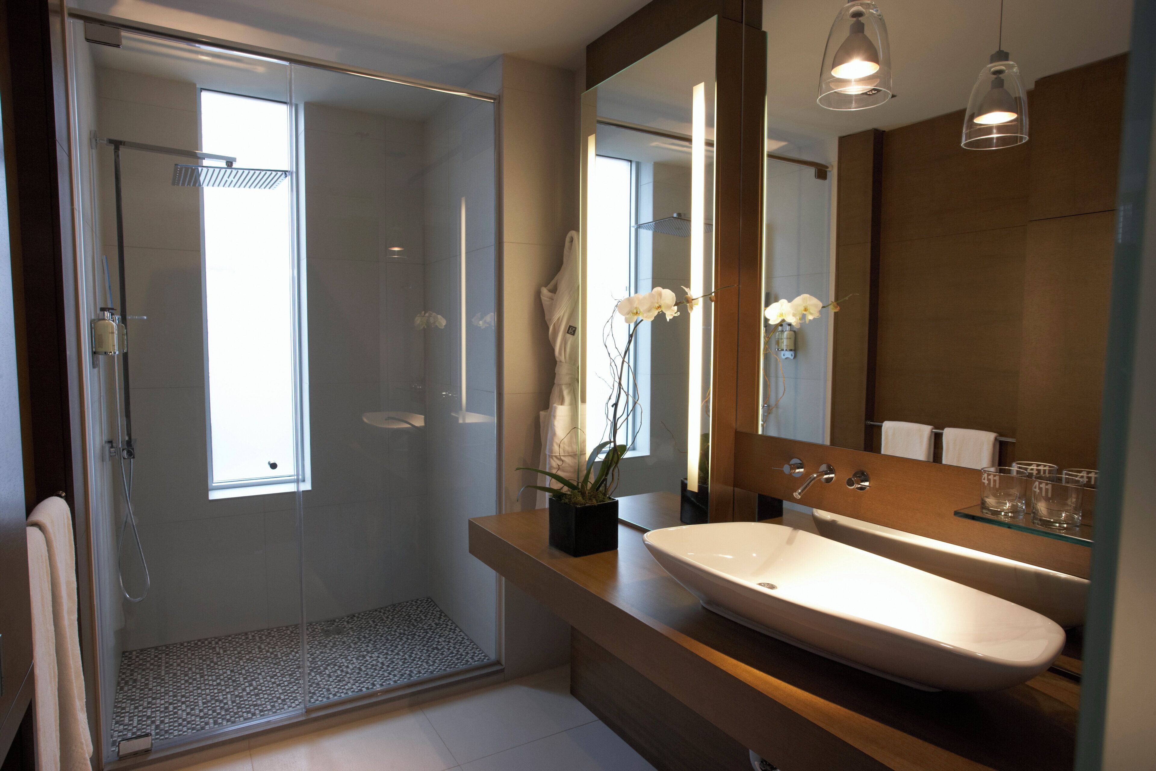 Un baño moderno con cabina de ducha de vidrio, un lavamanos grande de color blanco y un espejo con un estante de vidrio arriba.