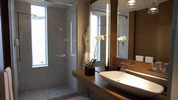 Un baño moderno con cabina de ducha de vidrio, un lavamanos grande de color blanco y un espejo con un estante de vidrio arriba.