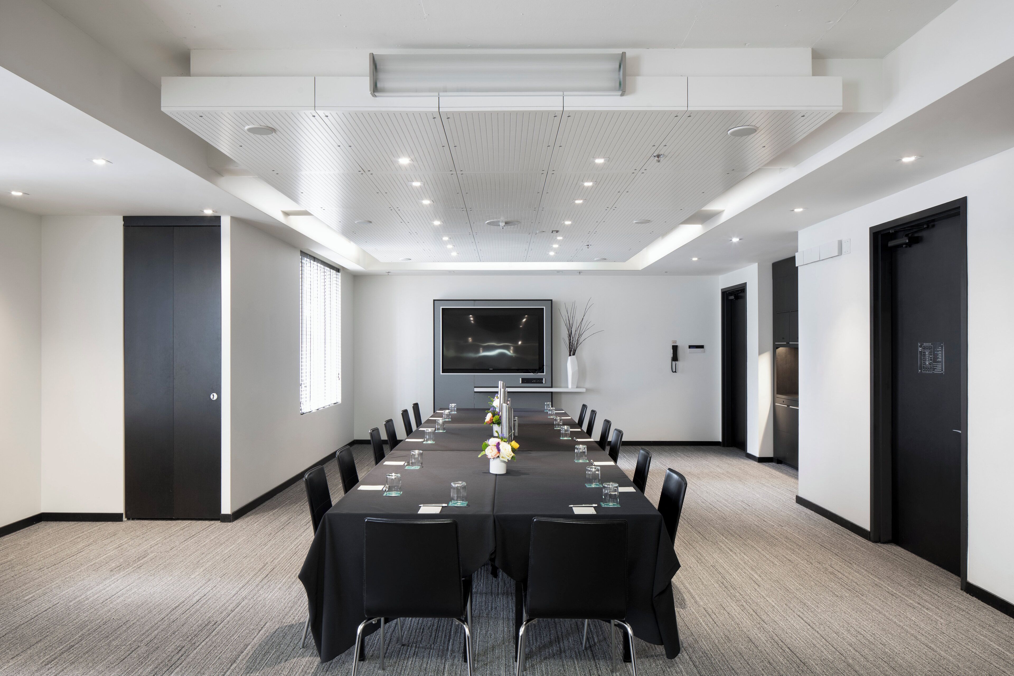 A conference room with a long table, chairs, a TV screen, and a modern ceiling design.