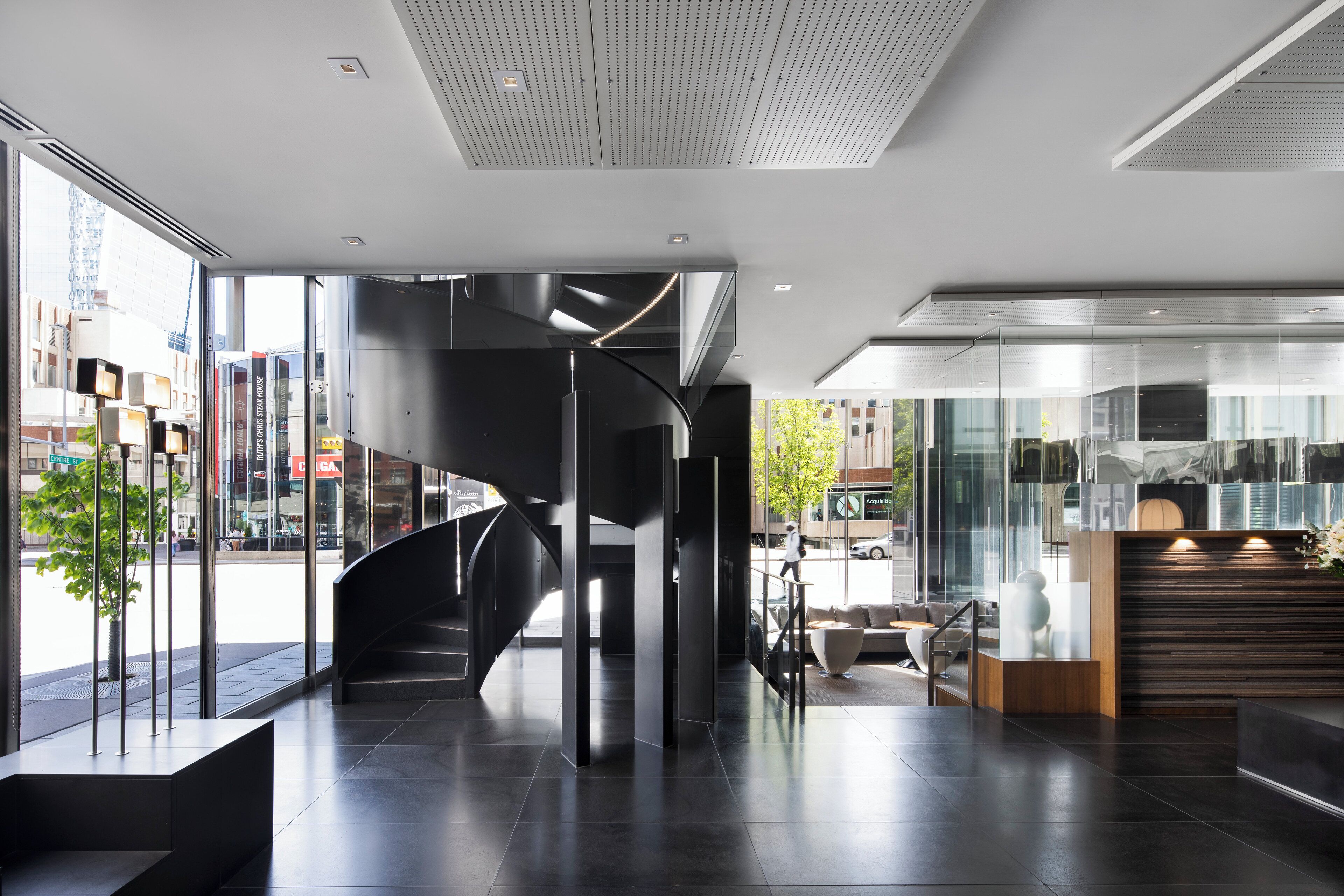 Un interior moderno con una escalera espiral, un mostrador de recepción y grandes ventanales que dan a la calle.